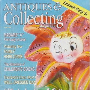 May include: The cover of "Antiques & Collecting Magazine" from June 2004 features a winking, smiling flower-faced ceramic figure. The magazine's title is in white letters on a light blue background. The cover also includes the text "Made in Japan Pottery."