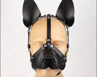May include: Black leather pup hood with attached ears and nose piece. The hood features adjustable straps and metal hardware. The word "TAVARON" is printed in a stylized font at the bottom of the image.