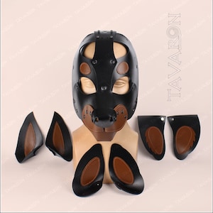 May include: A black leather dog mask with brown leather accents. The mask has a snout, ears, and eye holes. The mask is on a mannequin head. There are also four separate brown leather ear pieces.