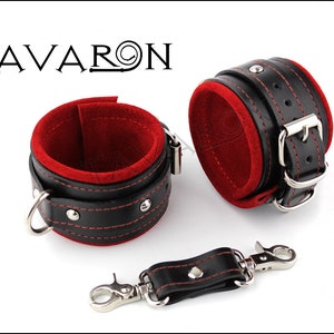 May include: A pair of black leather cuffs with red velvet lining and silver hardware. The cuffs are connected by a black leather strap with a silver hook.