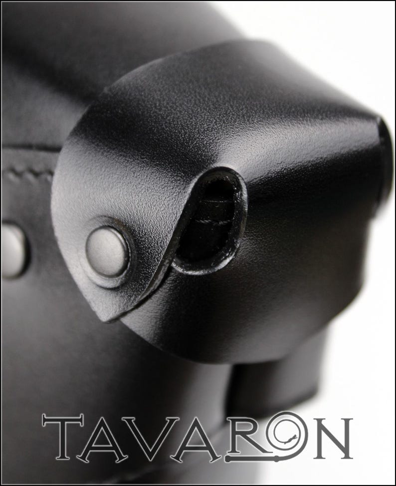 Puede incluir: Primer plano de un producto de cuero negro con una superficie texturizada. La imagen destaca las costuras, los remaches y una solapa curva asegurada con un broche. La palabra "TAVARON" est&aacute; impresa en una fuente serif en la parte inferior.
