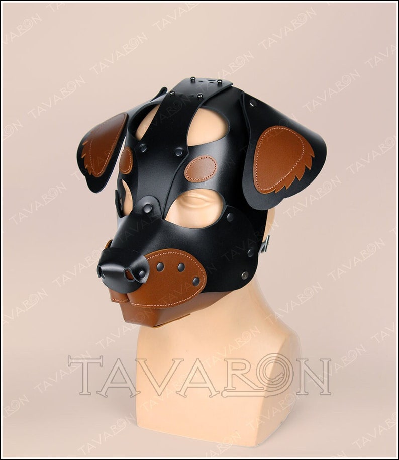 May include: A black leather dog mask with brown leather ears and nose. The mask has a strap that goes around the head and a buckle to fasten it.