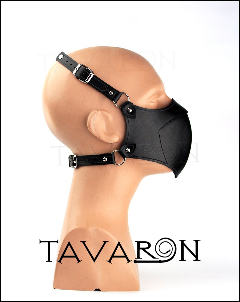May include: Black leather face mask with adjustable straps and metal hardware. The mask has a geometric design and is worn on a mannequin head.