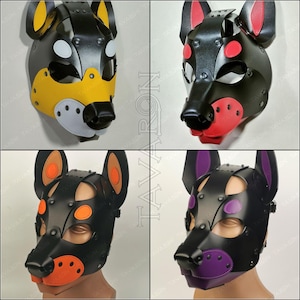 May include: Four black leather dog masks with different colored accents. The masks have a black leather base with a black metal nose and ears. The accents are yellow, red, orange, and purple.