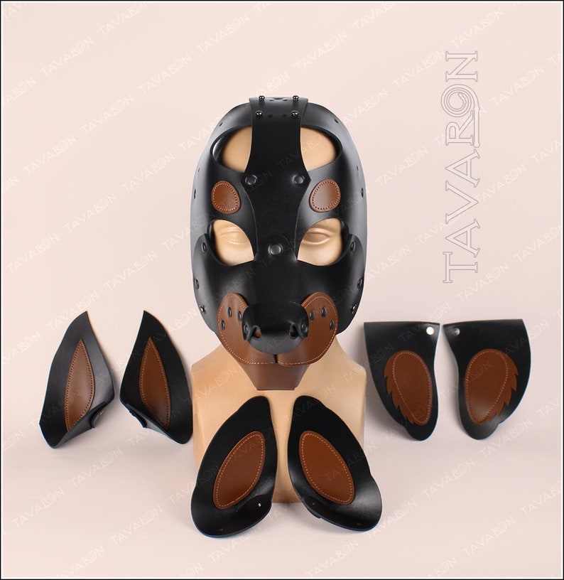 May include: A black leather dog mask with brown leather accents. The mask has a snout, ears, and eye holes. The mask is on a mannequin head. There are also four separate brown leather ear pieces.