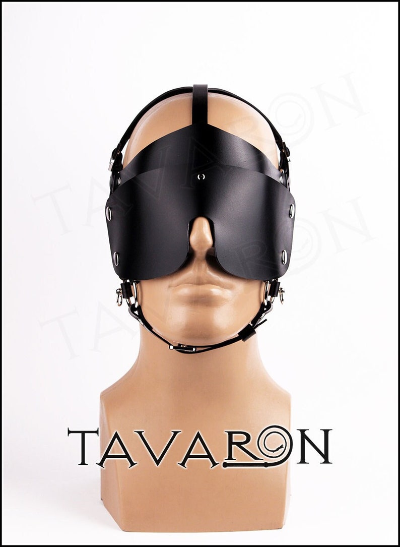 May include: Black leather blindfold with a head strap and a chin strap. The blindfold has a small opening for the nose. The blindfold is on a mannequin head.