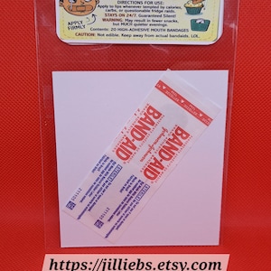 May include: A novelty diet aid patch kit in a clear plastic sleeve. The header card features a cartoon face with a taped mouth and text reading DIET AID PATCHES THE SHUT-CAKE-HOLE BAND-AID. Inside are two sterile Band-Aid brand adhesive bandages.