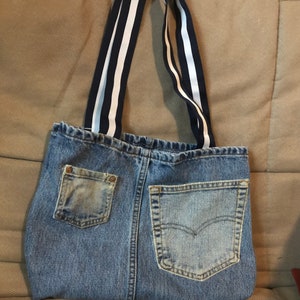 May include: A blue denim tote bag with two large pockets on the front. The bag has white and black striped straps.