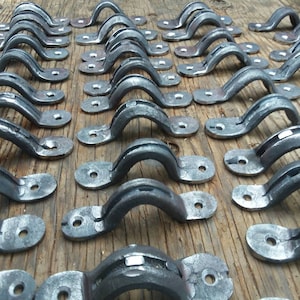 May include: A collection of metal drawer pulls in a silver finish. The pulls are shaped like a rounded arch with a flat base. They are arranged in rows on a wooden surface.