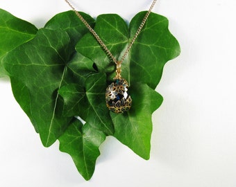 May include: A gold chain necklace with a black and gold pendant shaped like an egg with a floral design.