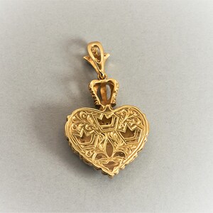 May include: A gold heart-shaped pendant with intricate floral designs and a crown at the top. The pendant is detailed with small, raised dots around the edges.