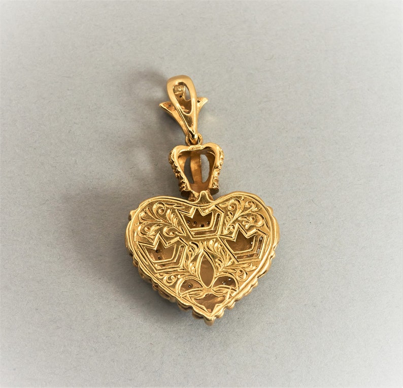 May include: A gold heart-shaped pendant with intricate floral designs and a crown at the top. The pendant is detailed with small, raised dots around the edges.