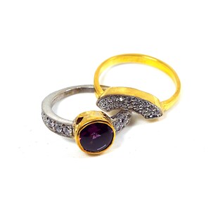 May include: Two gold rings with clear stones. One ring has a purple stone in the center.
