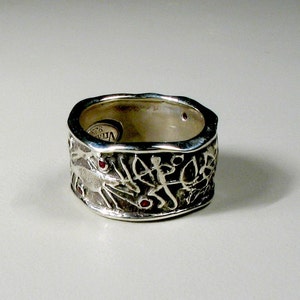 May include: A silver ring with intricate carvings and red gemstones. The ring is wide and has a textured surface.