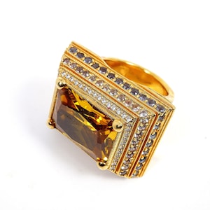 May include: A gold ring with a large, rectangular, brown gemstone surrounded by smaller, clear gemstones.