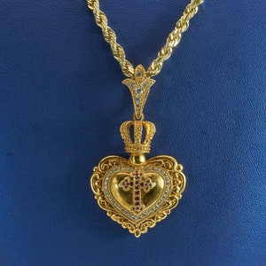 May include: A gold heart-shaped pendant with a crown and a cross set with red and white stones hangs from a gold rope chain.