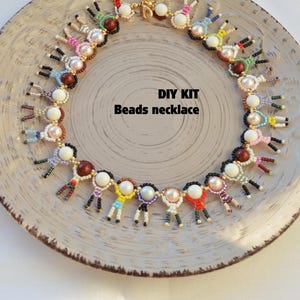 Könnte beinhalten: Eine handgefertigte Perlenkette mit einem einzigartigen Design. Die Kette zeigt kleine, farbenfrohe Figuren und besteht aus weißen und perlenartigen Perlen. Der Text "DIY KIT Beads necklace" ist sichtbar.