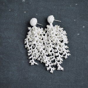 May include: A pair of white beaded dangle earrings with silver accents. The earrings are long and have a cascading design.