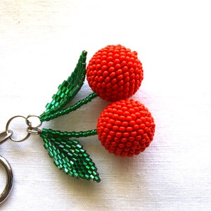 May include: A red beaded cherry keychain with green beaded leaves.