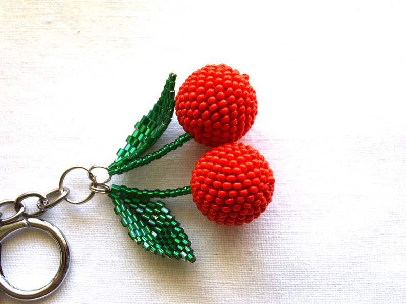 May include: A red beaded cherry keychain with green beaded leaves.