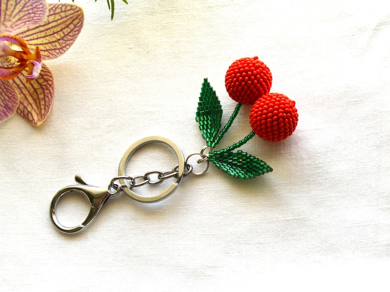 May include: A silver key chain with a beaded cherry charm. The charm features two red cherries with green leaves.