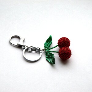 May include: A silver key chain with a beaded cherry charm. The cherry is red and has green leaves.