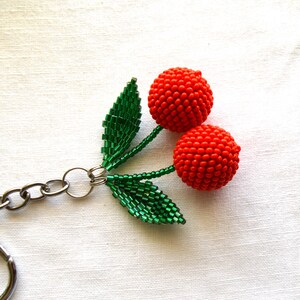 May include: A beaded cherry keychain with a silver chain and green leaves. The cherries are red and made of small beads.