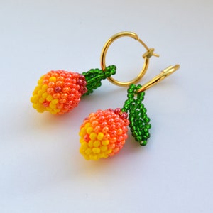 May include: A pair of gold hoop earrings with beaded peach charms. The charms are made of orange, yellow, and green beads and resemble small peaches.