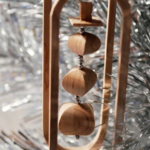 May include: Wooden Christmas ornament with a geometric design and a series of wooden spheres hanging inside. The spheres are connected by silver beads.