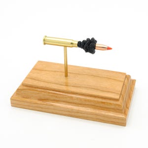 Könnte beinhalten: Dekorative Präsentation mit einer Messingkugel mit roter Spitze, gehalten von einem goldfarbenen Ständer auf einem Holzsockel. Die Kugel ist teilweise in schwarzes Material eingewickelt. Der Holzsockel hat ein mehrstufiges Design.