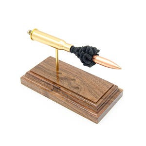 Könnte beinhalten: Eine dekorative Skulptur mit einer Messingkugel mit Kupferspitze, verziert mit einem schwarzen Perlenakzent. Die Kugel ist auf einem goldenen Ständer montiert und steht auf einem rechteckigen Sockel aus dunklem Holz.