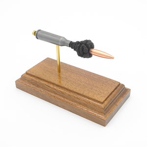 Op de afbeelding: Een decoratieve sculptuur met een kogelvormig object met een koperen punt, vastgehouden door een zwart, getextureerd element. Het is gemonteerd op een houten voet met een messingkleurige steun. De voet is donkerbruin.