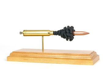Puede incluir: Una vaina de bala de latón y cobre montada en una base de madera con un cepillo de limpieza negro unido al extremo.