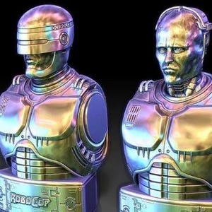May include: Two metallic silver and iridescent bust sculptures of Robocop, a fictional cyborg police officer. The sculptures are detailed and feature a metallic finish.