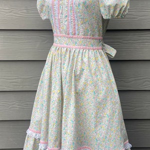 Puede incluir: Un vestido blanco con estampado floral y detalles en rosa. El vestido tiene un ribete de encaje y una falda con volantes.