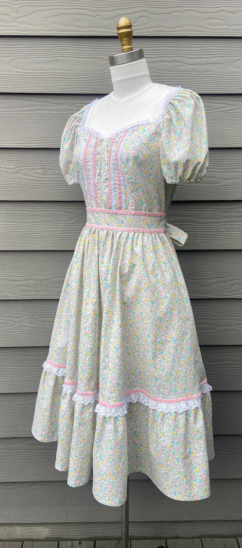 Puede incluir: Un vestido blanco con estampado floral y detalles en rosa. El vestido tiene un ribete de encaje y una falda con volantes.