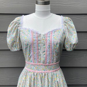 Puede incluir: Un vestido vintage floral con ribete de encaje rosa y blanco, mangas abullonadas y un corpi&ntilde;o ajustado. El vestido tiene un fondo verde claro con un peque&ntilde;o estampado floral.