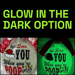 May include: A Christmas ornament with the text "he Sees YOU When you're Pooping." The ornament has a Santa hat graphic and a red ribbon. The image also shows the ornament glowing green in the dark, with the text "GLOW IN THE DARK OPTION."