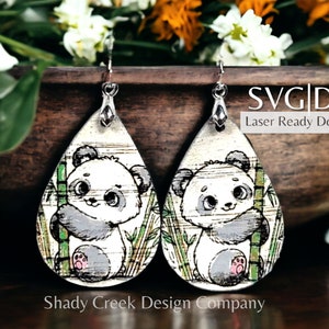May include: A pair of teardrop-shaped earrings featuring a panda bear design. The panda is holding onto a bamboo stalk and is surrounded by bamboo leaves. The earrings are laser-cut and ready to be downloaded. SVG | DXF Laser Ready Download