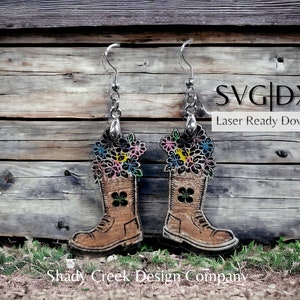 Puede incluir: Un par de pendientes de madera con forma de botas con flores en la parte superior. Los pendientes son marrones con un diseño de trébol negro y cuelgan de ganchos plateados. El texto "SVG|DXF Laser Ready Download" es visible en la imagen.