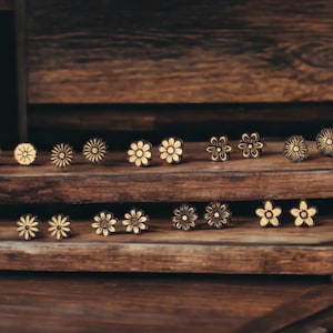 May include: A display of wooden flower earrings with a light brown wood base and white flower designs. The earrings are arranged in two rows on the wooden base.