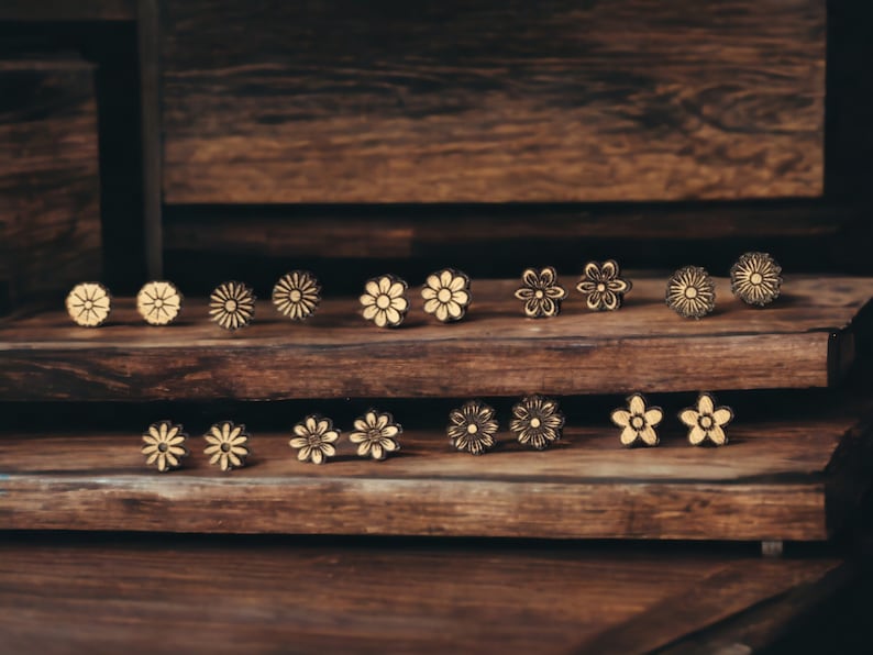 May include: A display of wooden flower earrings with a light brown wood base and white flower designs. The earrings are arranged in two rows on the wooden base.