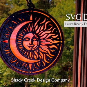 May include: A black and orange sun and moon design with a face on the sun. The design is cut out of wood and is ready to be used for laser cutting. The text "SVG|DXF Laser Ready Download" is in the top right corner of the image.