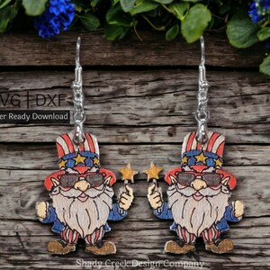 May include: A pair of wooden earrings featuring a gnome wearing a red, white, and blue hat and sunglasses. The gnome is holding a star-shaped wand. The earrings are laser cut and ready to download. SVG + DXF. Laser Ready Download.