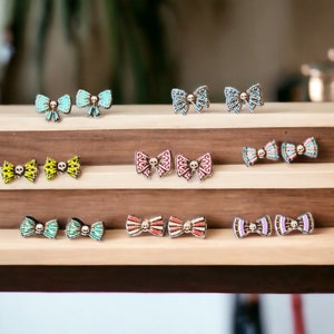 May include: A display of colorful bow-shaped earrings with skull details. The earrings are arranged on a wooden shelf with multiple tiers.