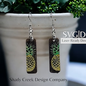 May include: A pair of brown wooden earrings with a pineapple design. The earrings are laser cut and ready to download. SVG and DXF files are included. Shady Creek Design Company.