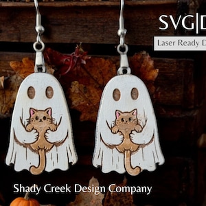May include: A pair of wooden earrings featuring a white ghost holding a brown and white cat. The earrings are laser cut and ready to be assembled.  SVG|DXF Laser Ready Download. Shady Creek Design Company.