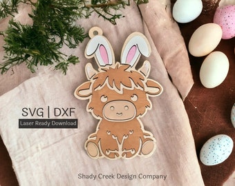 May include: A brown Highland cow with bunny ears, a laser-cut wooden ornament. The ornament is on a light brown fabric background with a white text overlay that says "SVG | DXF Laser Ready Download" and "Shady Creek Design Company".