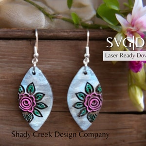 May include: A pair of silver earrings with a floral design. The earrings are shaped like a teardrop and have a pink and green rose with leaves. The earrings are laser cut and ready to download. SVG | DXF Laser Ready Download Shady Creek Design Company