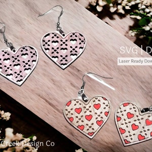 May include: A pair of laser cut wooden earrings in the shape of a heart with a smaller heart pattern. The earrings are on a wooden surface with the text "SVG | DXF Laser Ready Download" above them.